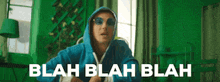 a man wearing a blue hoodie and sunglasses is standing in a green room .