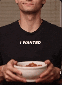a man wearing a black shirt that says " i wanted " holds a bowl of food