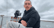 a man is sitting on a boat with a motor behind him and the words ' vido al ' on the bottom