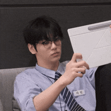 a man wearing glasses and a name tag that says 사원 looks at a tablet