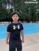 a boy in a black under armour shirt stands in front of a pool