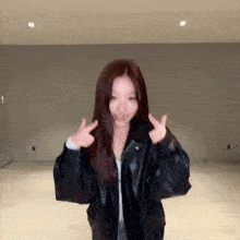 a woman is wearing a black leather jacket and making a peace sign .