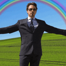 a man in a suit and tie is standing in a field with his arms outstretched in front of a rainbow