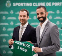 a man in a suit holds up a green super bock jersey