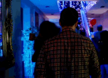 a man in a plaid shirt stands in a dark room