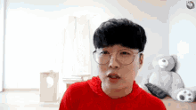 a young man wearing glasses and a red shirt is standing in front of a teddy bear