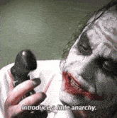 a man in a joker costume is talking on a cell phone and says introduce a little anarchy