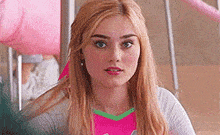 a young woman with long blonde hair is sitting in a classroom wearing a pink shirt .