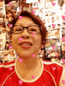 a woman wearing glasses and a red shirt is smiling in front of a wall full of pictures