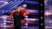 a man is carrying a woman in a red dress on his shoulders on a stage with a nbc logo in the background