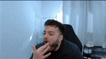 a man with a beard is yawning while sitting in a chair in front of a white wall .