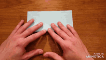 a person 's hands folding a piece of blue paper with the words made in animotica on the bottom