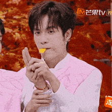 a man wearing a pink vest is holding a piece of food in his mouth