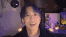 a young man with blue hair is smiling and looking at the camera in a room .
