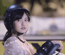 a woman wearing a helmet and holding a skateboard looks at the camera .