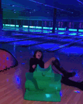 a woman is sitting on a green toy tank in a bowling alley