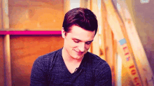 a young man in a gray shirt is smiling and looking down .