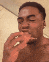 a shirtless man eating a slice of pizza