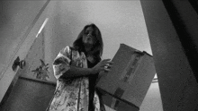 a black and white photo of a woman holding a cardboard box with a sticker that says fragile