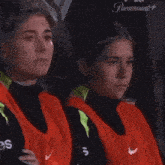two women wearing orange nike vests are sitting next to each other and smiling