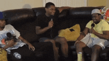 three men are sitting on a couch one is holding a microphone