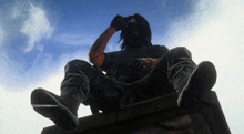 a statue of a man sitting on a ledge with a blue sky in the background