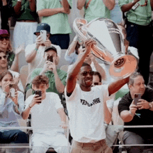 a man in a triumphe shirt holds up a trophy in front of a crowd of people