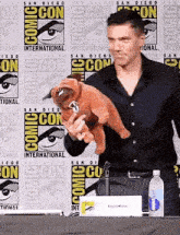 a man holding a stuffed animal in front of a comic con wall