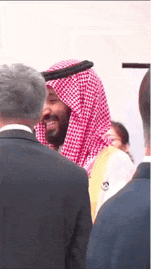a man in a red and white checkered keffiyeh smiles while standing in a crowd