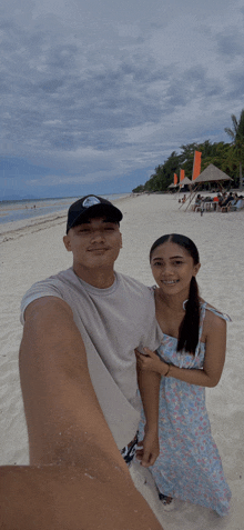 a man and a woman are posing for a selfie on a beach