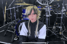 a woman with long blonde hair is sitting in front of a drum set and wearing a black and white jacket that says duke