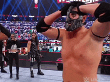 a shirtless wrestler wearing a mask stands in front of a crowd