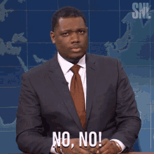 a man in a suit and tie says " no no " in front of a map
