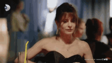 a woman in a black dress is sitting at a table with a yellow straw in her hand