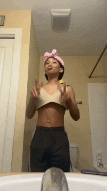 a woman wearing a crop top and a pink headband stands in front of a bathroom sink