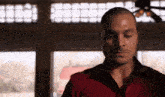 a man wearing a red shirt is standing in front of a window .