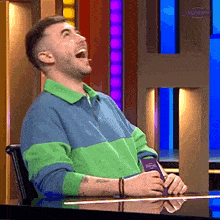 a man in a green and blue sweater is sitting at a table laughing .