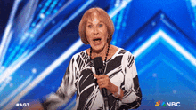 an older woman singing into a microphone with a nbc logo in the corner