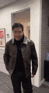 a man in a brown leather jacket is standing in a hallway with his hands in his pockets