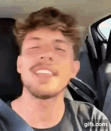 a man with a beard is sitting in the back seat of a car with his eyes closed and smiling .