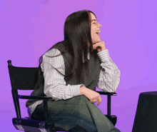 a woman is sitting in a director 's chair with her arms outstretched and laughing