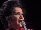 a woman singing into a microphone with a man playing a violin in the background