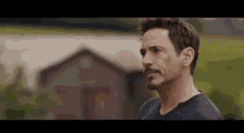tony stark is standing in front of a barn in a field .