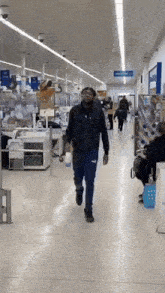 a man in a black jacket and blue pants is walking down a store hallway
