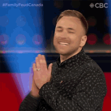 a man in a black shirt is clapping his hands while smiling .
