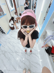 a girl wearing sunglasses and a pink hat has a smiley face on her mouth