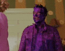 a man with purple paint on his face stands next to a woman in a pink shirt
