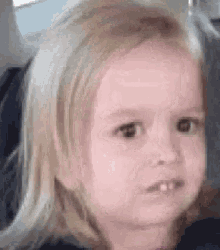 a little girl with blonde hair is making a funny face with her mouth open .