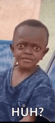 a little boy in a blue shirt is making a funny face and saying huh ?