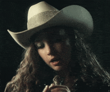 a woman wearing a white cowboy hat is singing into a microphone